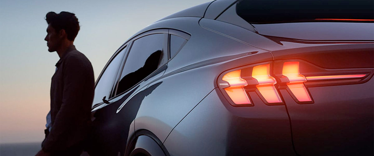 Partial rear view of a 2021 Ford Mustang Mach E at night with a man leaning against the door and taillamps illuminated