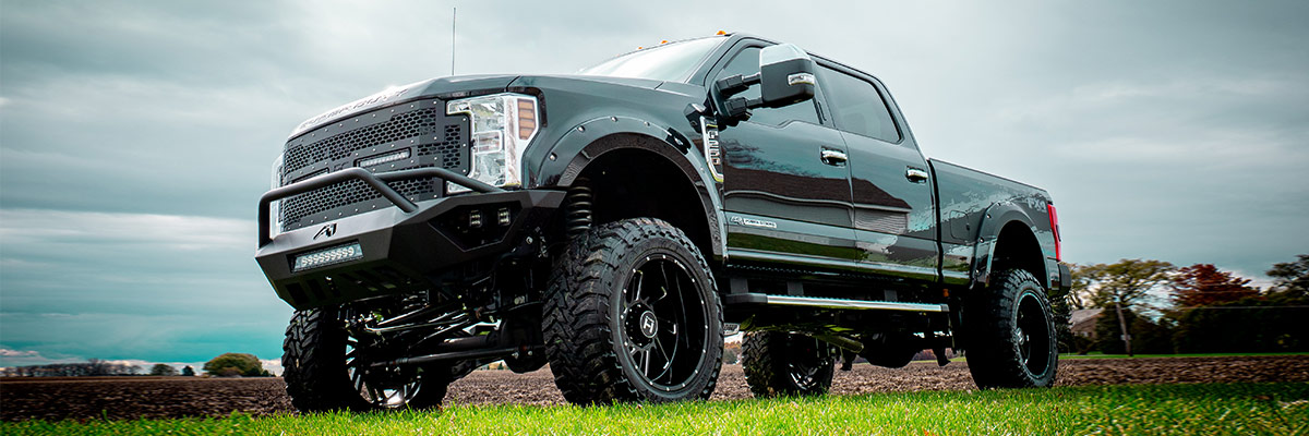 side view of Ford F-350 lifted truck with black tire rims on a a open field