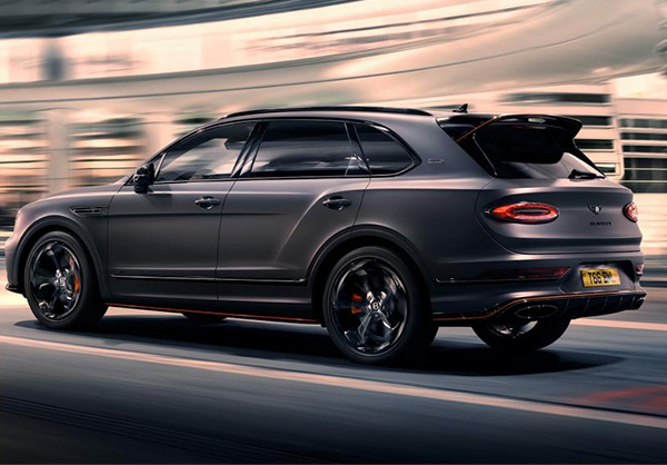 Bentley Bentayga S Black Edition driving dynamically through a city featuring 22 inch S directional wheel - Black Painted and Polished as well as Mandarin accents on the styling kit
