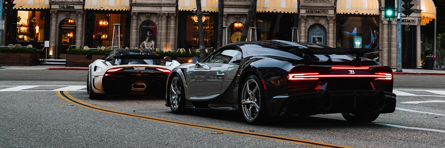 Two luxuy vehicles going through a green light in the city