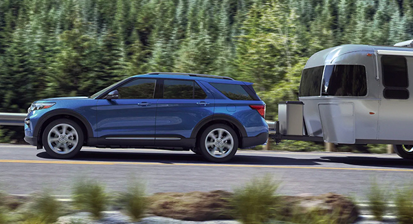 A 2020 Ford Explorer Hybrid in Atlas Blue towing a camper on the highway