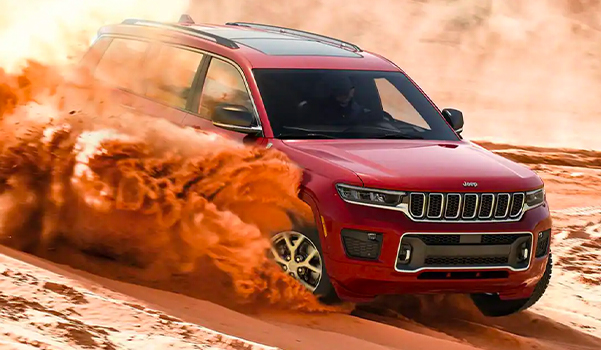 A 2021 Jeep Grand Cherokee L Overland rapidly descending a sandy hill, with dust and smoke billowing from the front and rear tires.