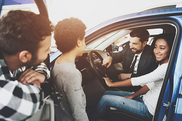 Family at car dealership. Salesman is showing new car.