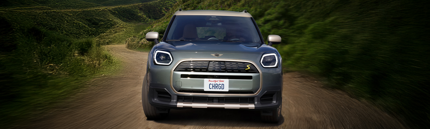 Front-view of a 2025 MINI Countryman SE ALL4 driving up a dirt road in a mountainous region.